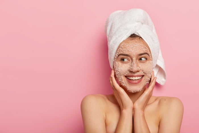 ragazza che sorride mentre fa uno scrub viso - esfoliazione meccanica